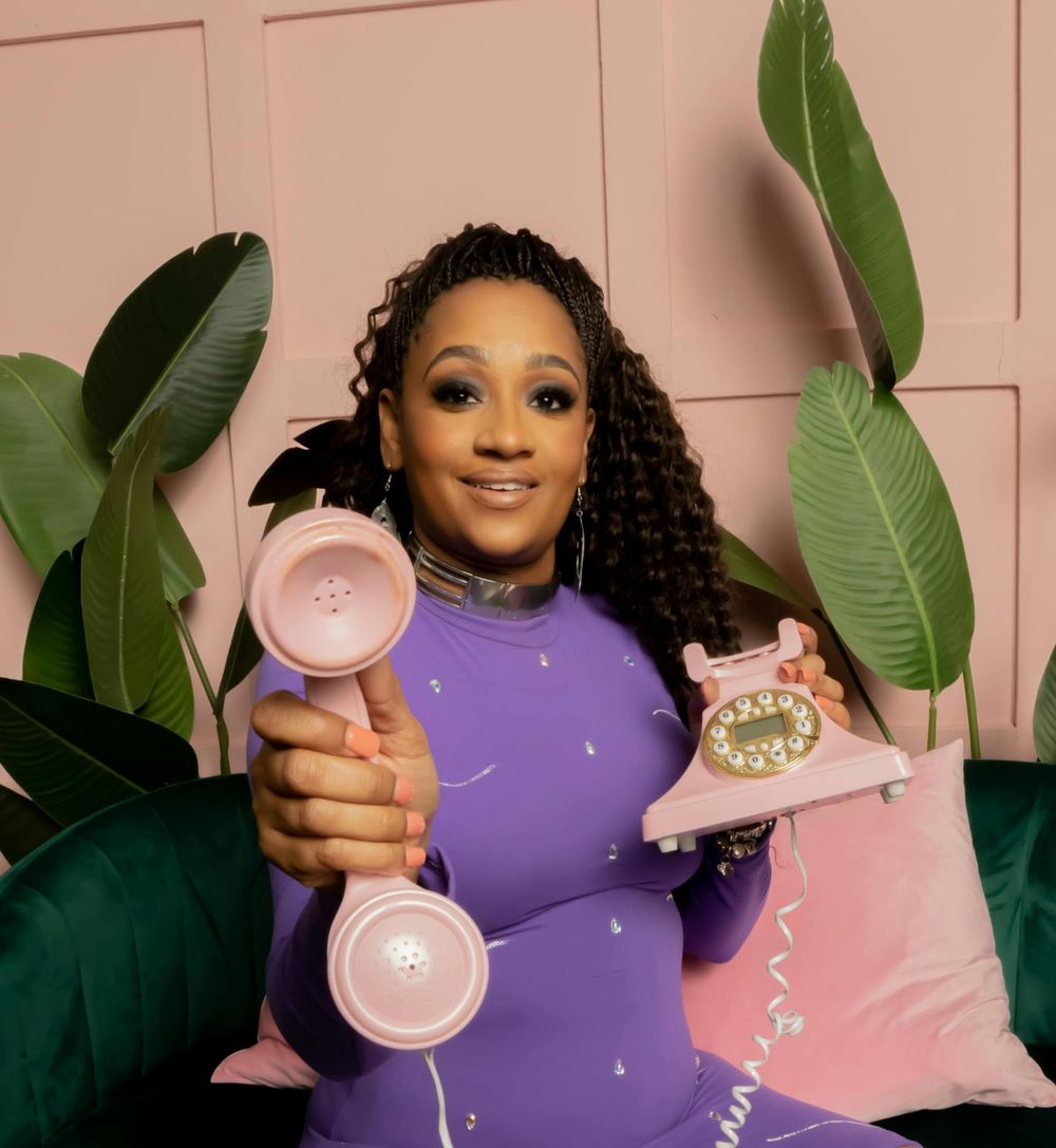 A smiling team member holds two retro pink telephones, ready to take your call