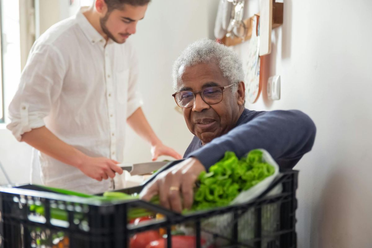 A younger man helps an older man unpack fresh groceries